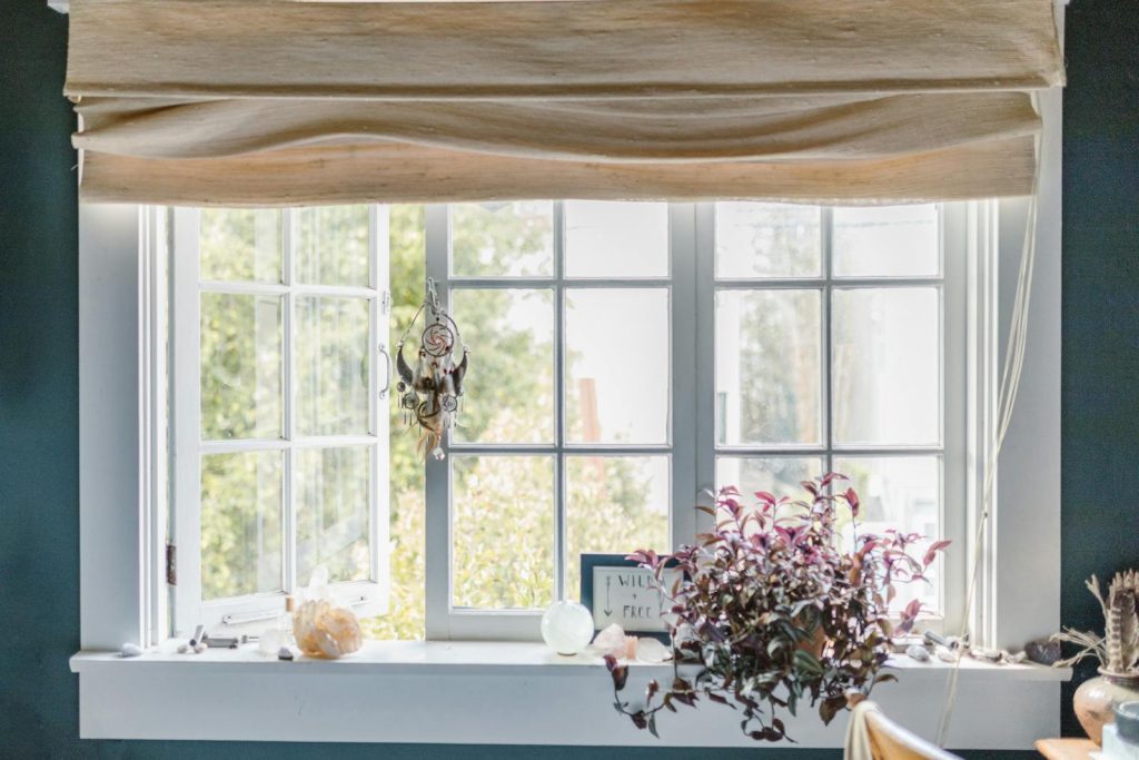 A serene indoor window scene with a dreamcatcher, crystals, and potted plant.